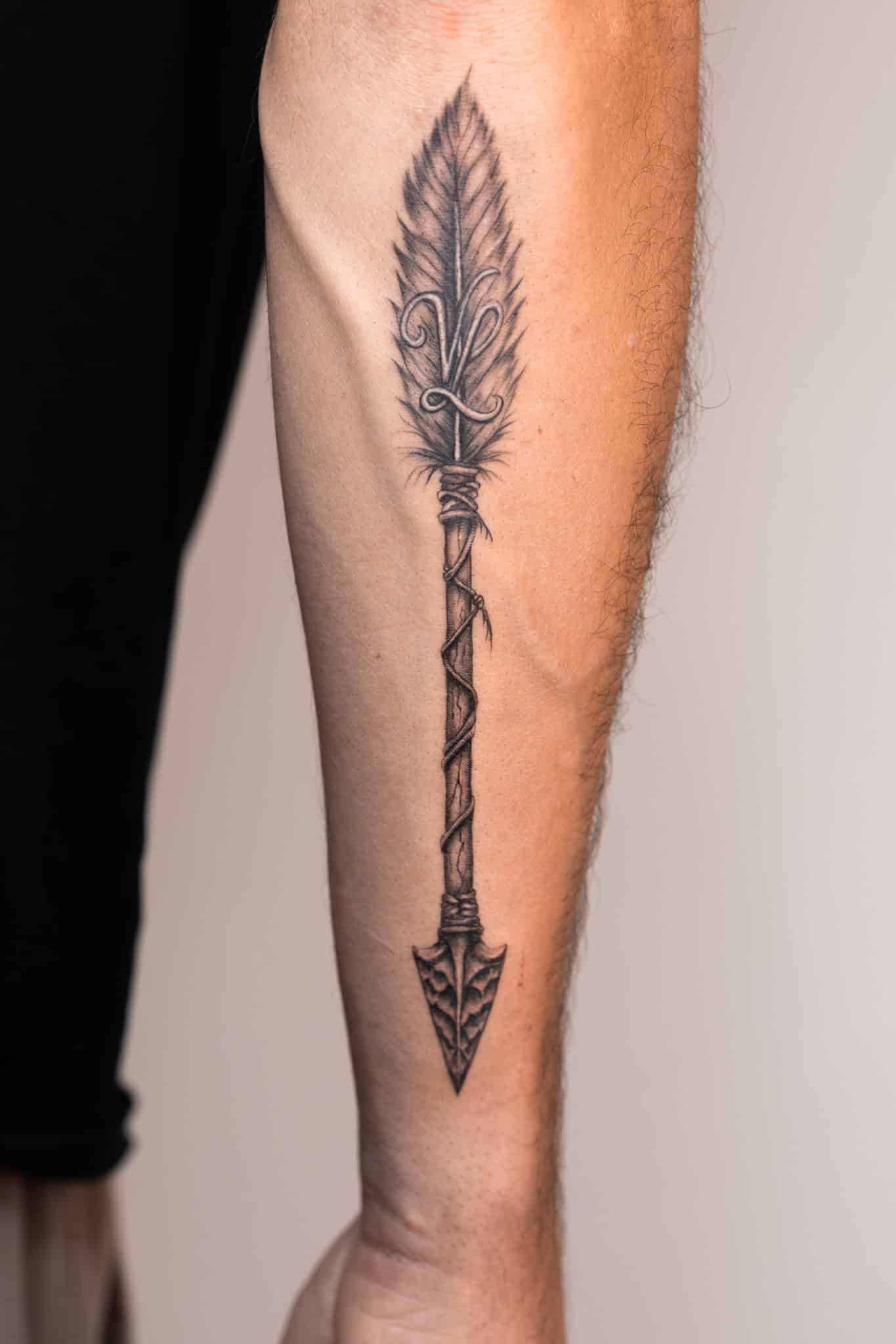 Tatouage flèche et plume réaliste noir et gris sur l’avant-bras