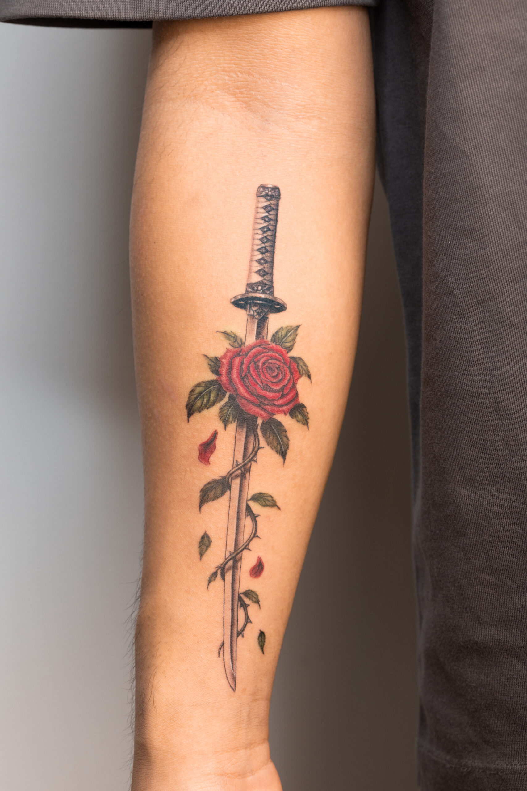Tatouage katana avec rose rouge et feuillage sur l’avant-bras